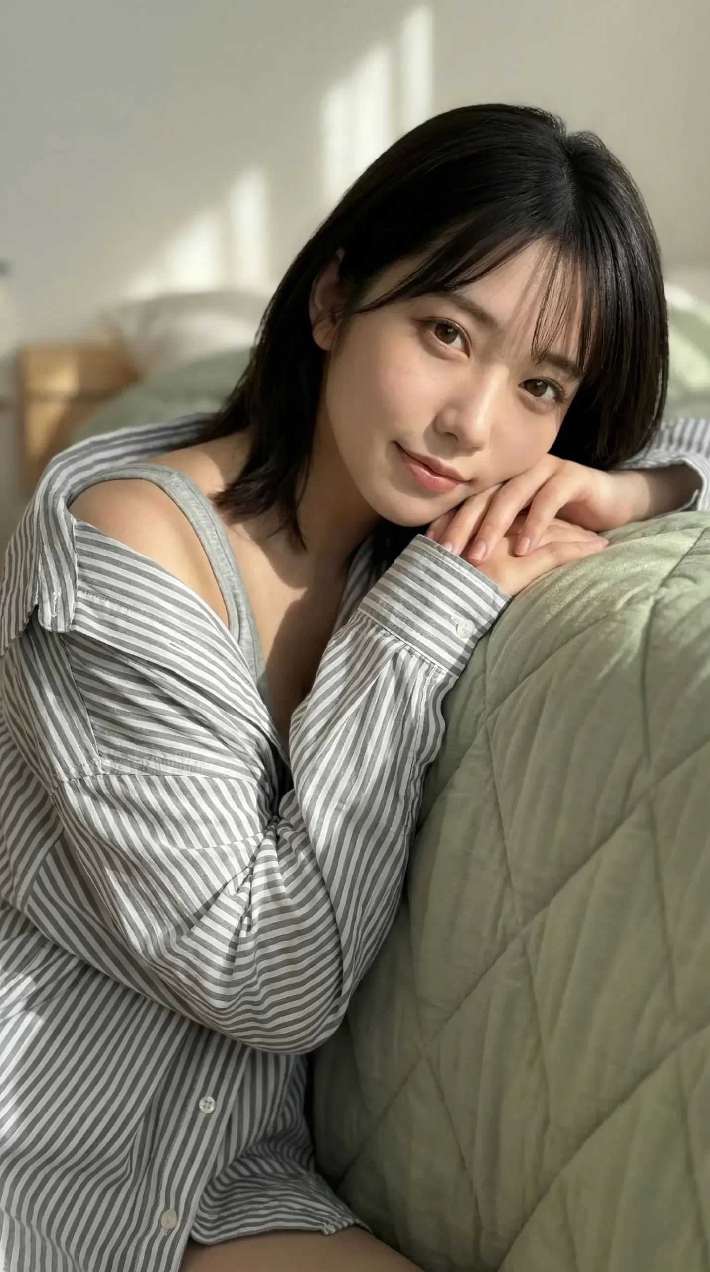 ベッドでくつろぎ、こちらを見つめて優しく微笑むストライプシャツ姿の女性
