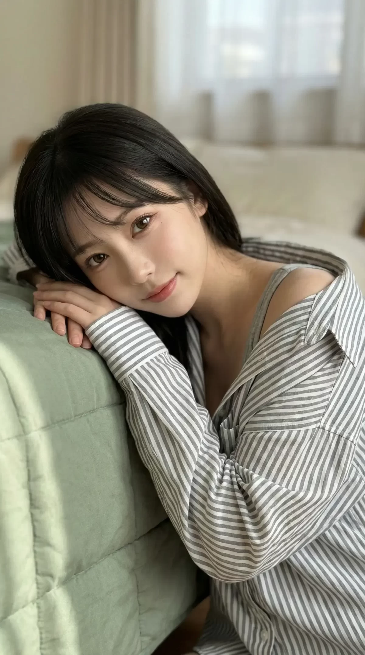 ストライプ柄のシャツを着た黒髪の女性が、クッションに寄りかかりこちらを見つめる。
