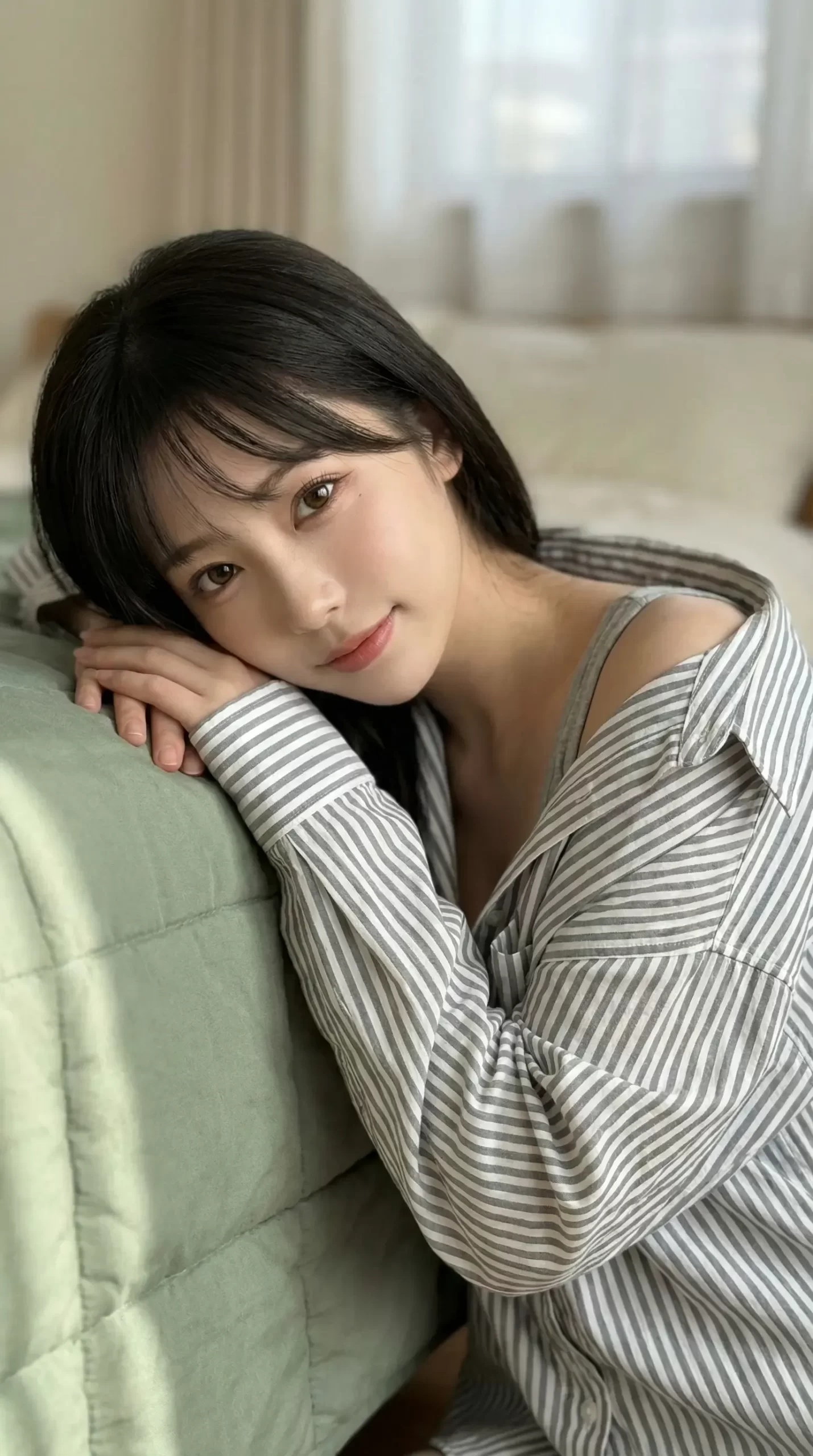 ストライプ柄のシャツを着た黒髪の女性が、クッションに寄りかかりこちらを見つめる。
