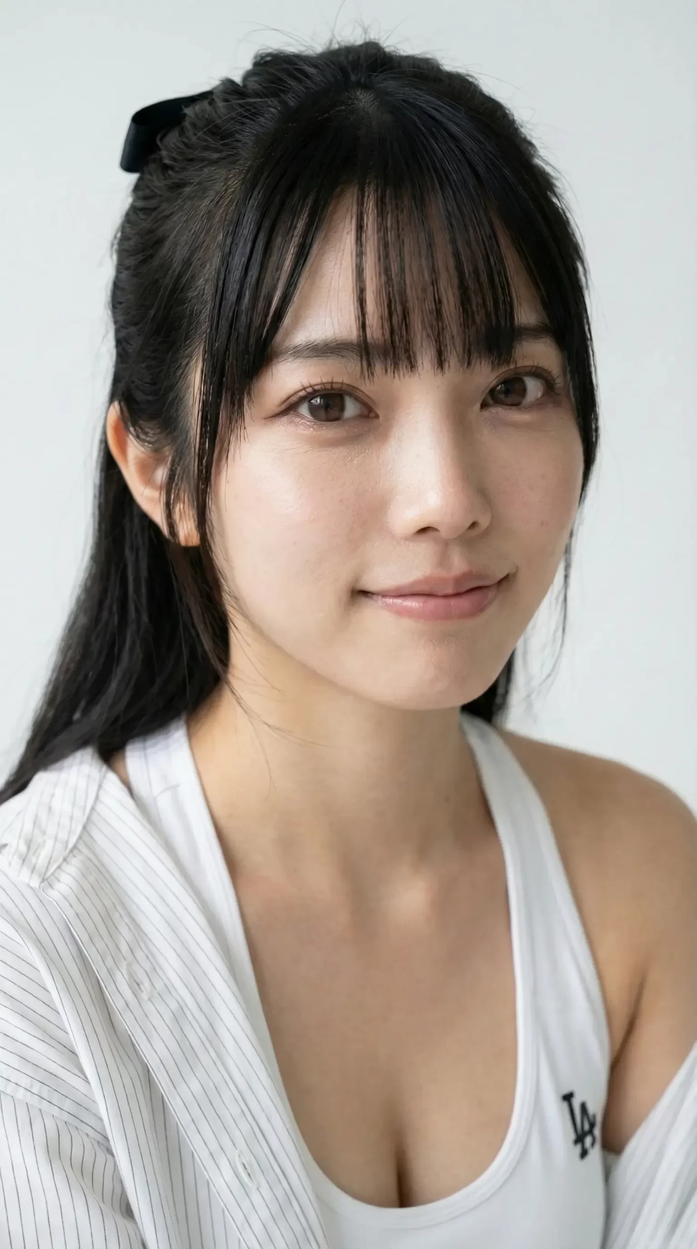 黒髪で前髪のある女性が、白いタンクトップとシャツを着用し、こちらを向き微笑む姿。