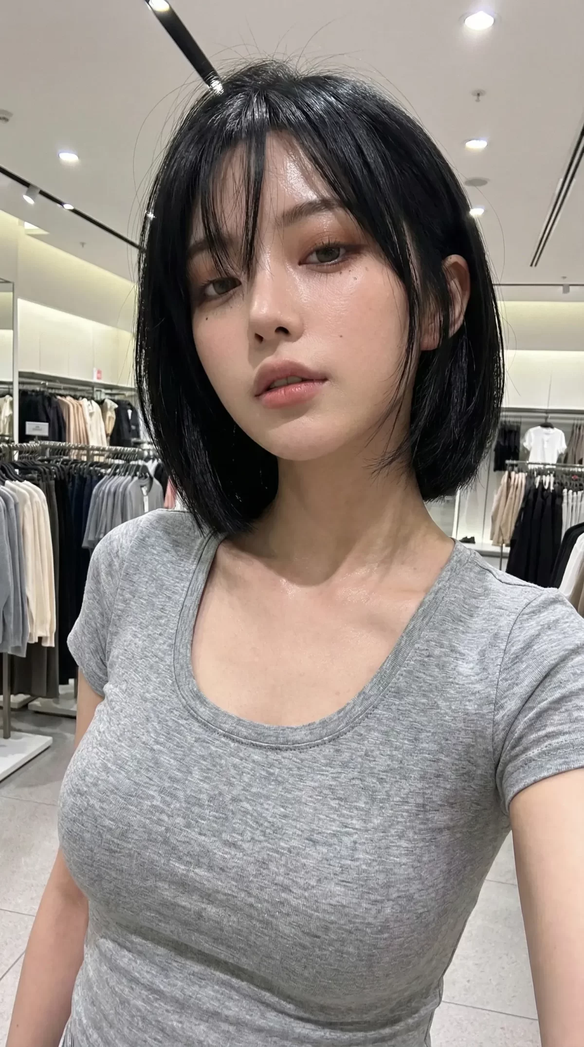 グレーのTシャツを着た黒髪ボブの女性が、アパレル店内で正面を見つめる姿