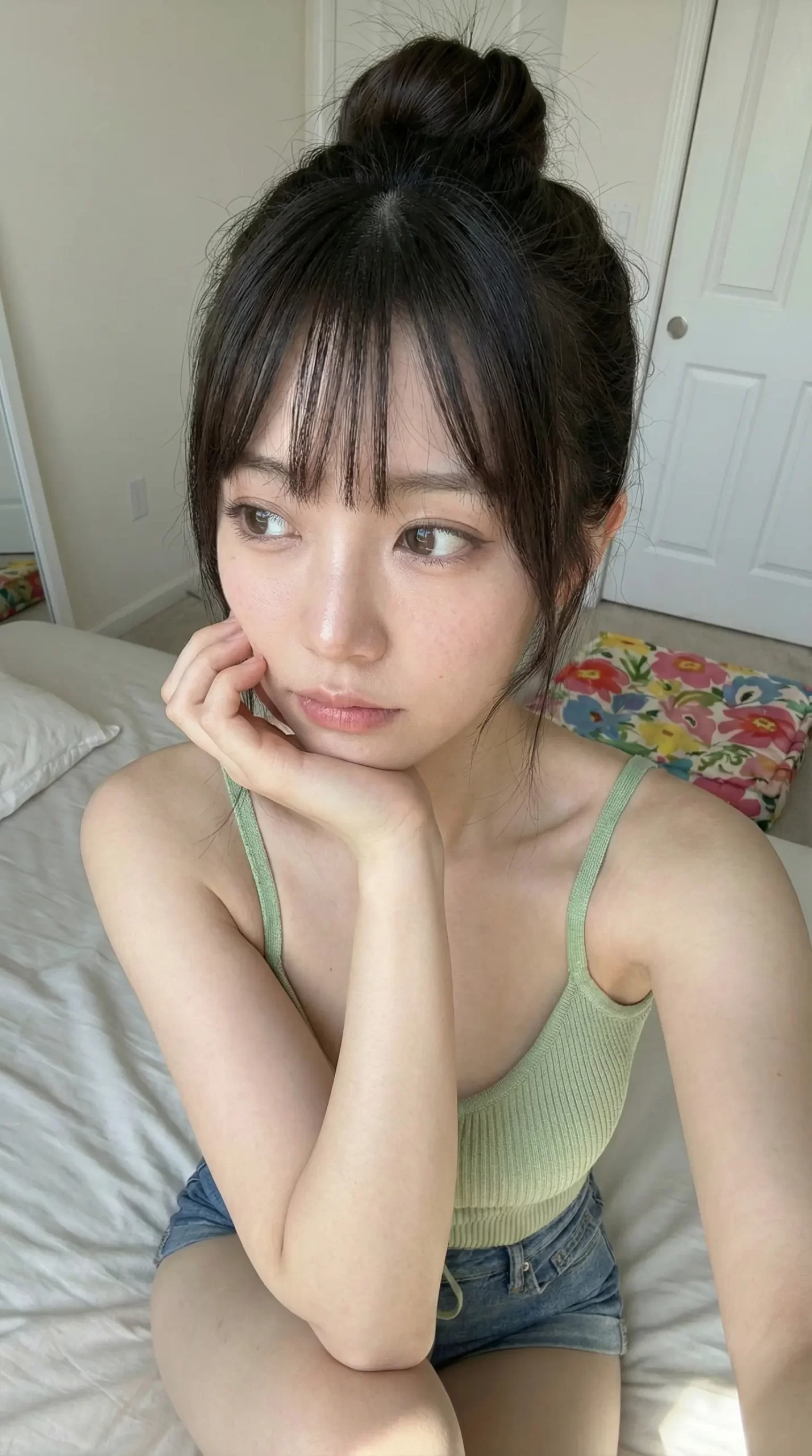 薄緑のキャミソール姿で、ベッドの上で頬杖をつき遠くを見つめるお団子ヘアの女性