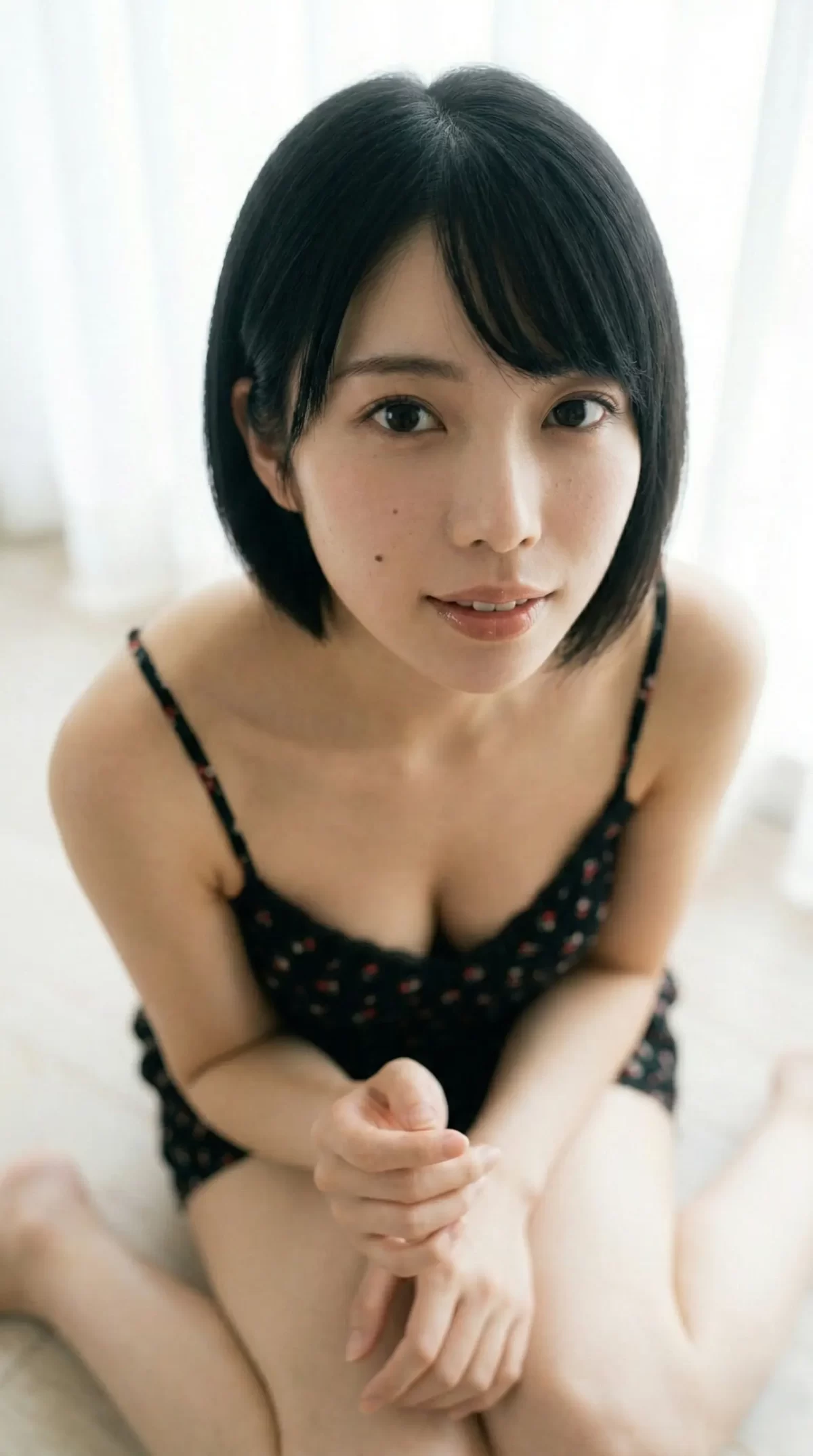 黒いキャミソール姿で床に座り、穏やかにカメラを見上げるショートヘアの女性