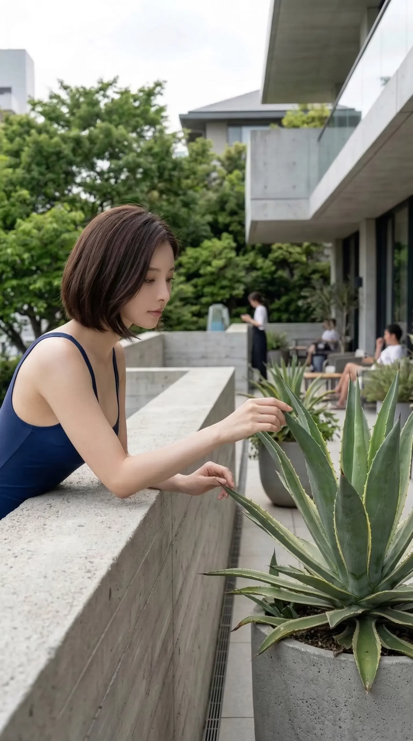 ネイビーのキャミソールを着た女性が、テラスでアガベの葉に触れている。