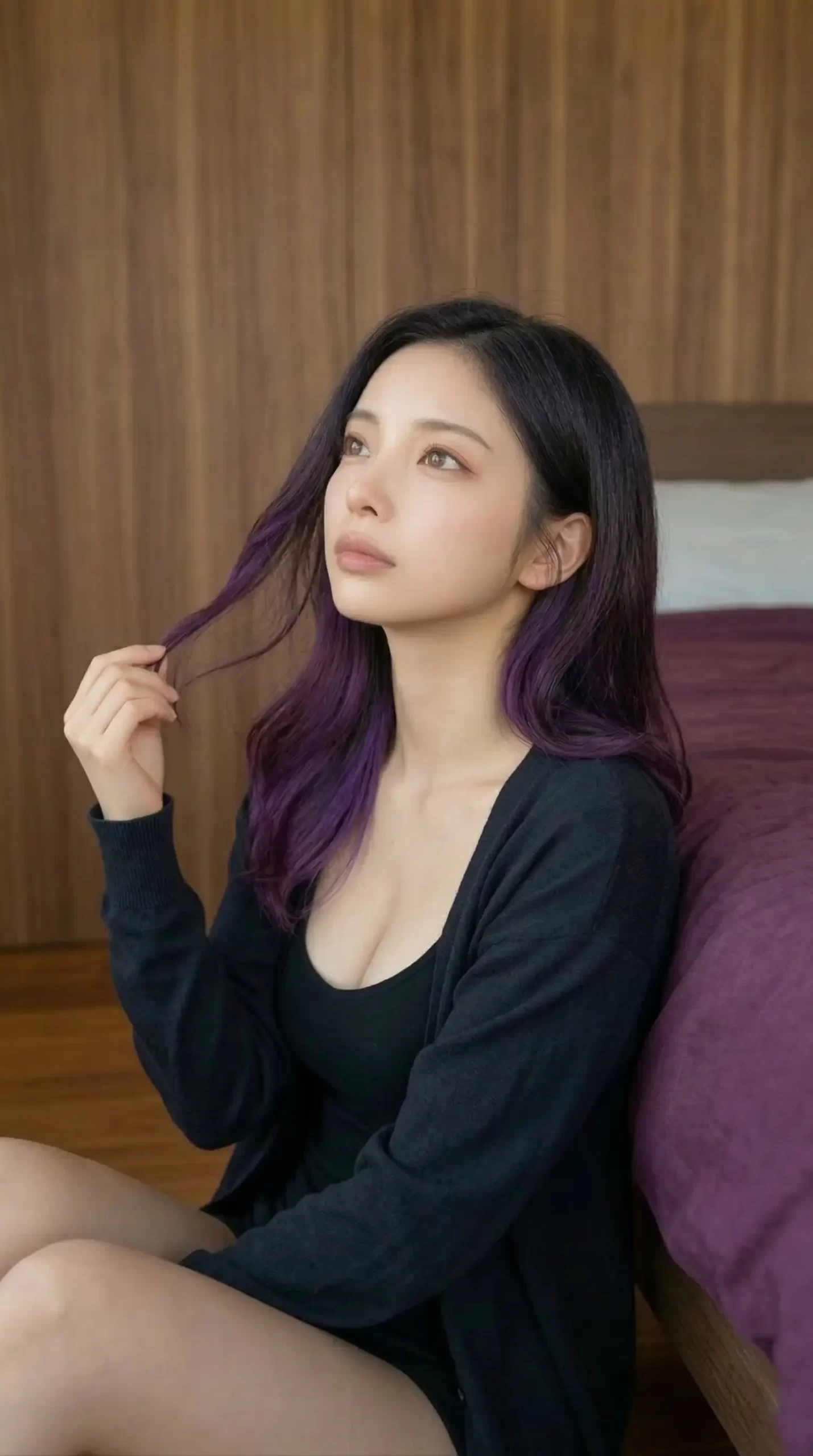 毛先が紫色のロングヘアの女性が、黒い服を着てベッドの横に座り上を見つめています。