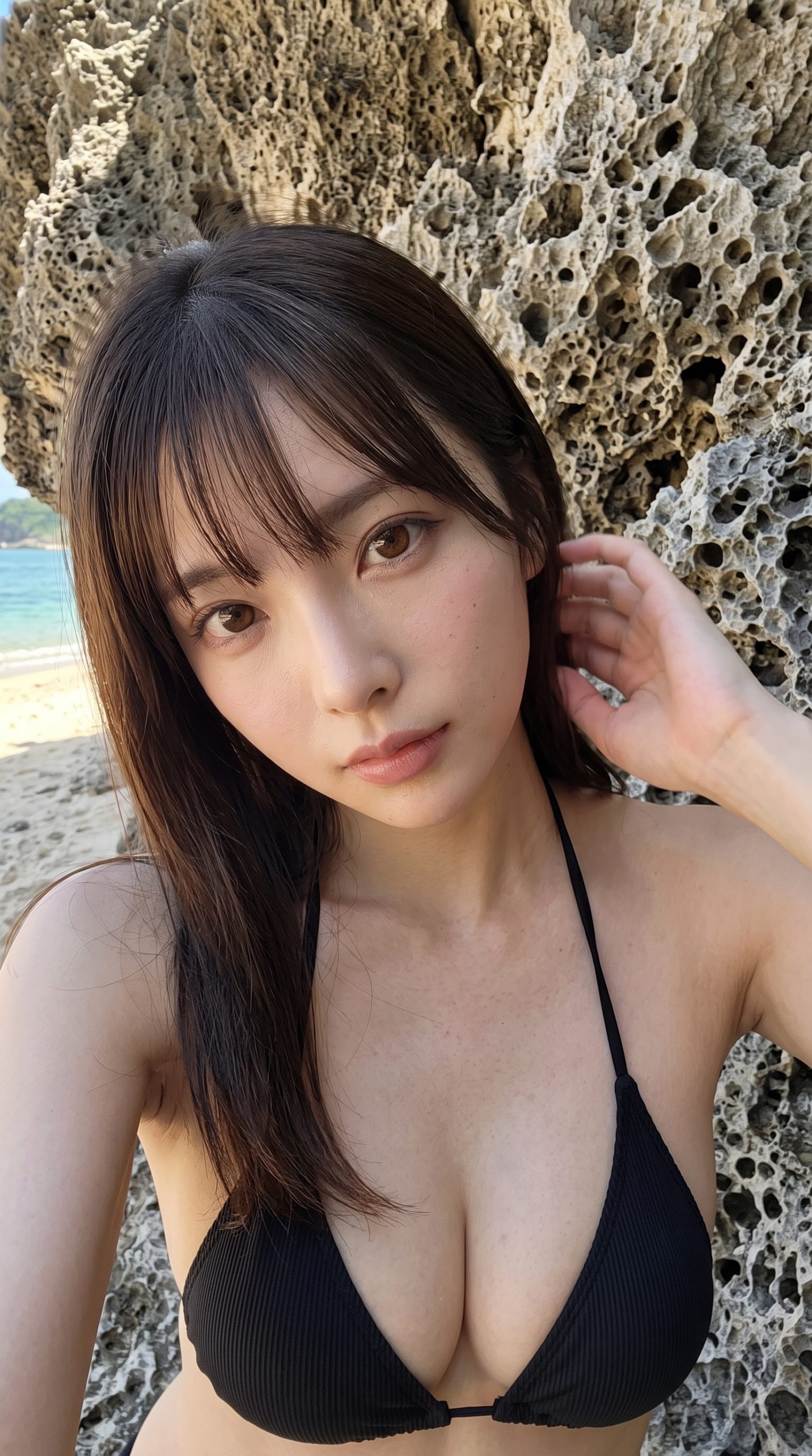 海辺の岩場を背景に、黒い水着を着てカメラを見つめる女性。