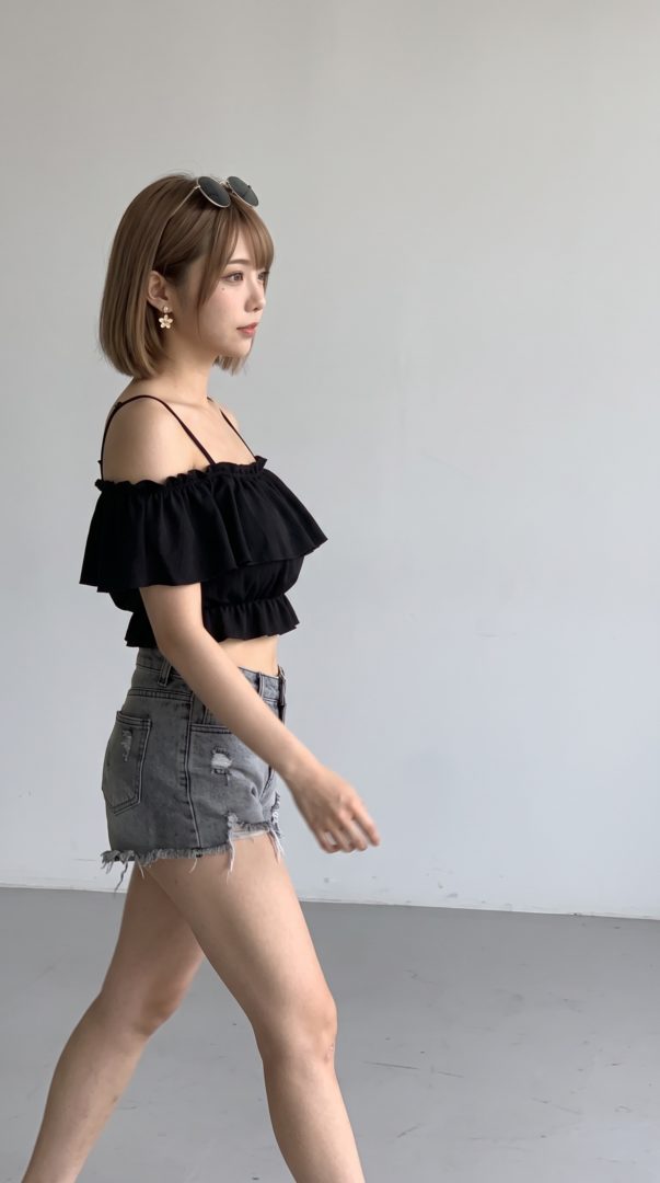 黒のオフショルダートップスとデニムショートパンツを着て歩くボブヘアの女性