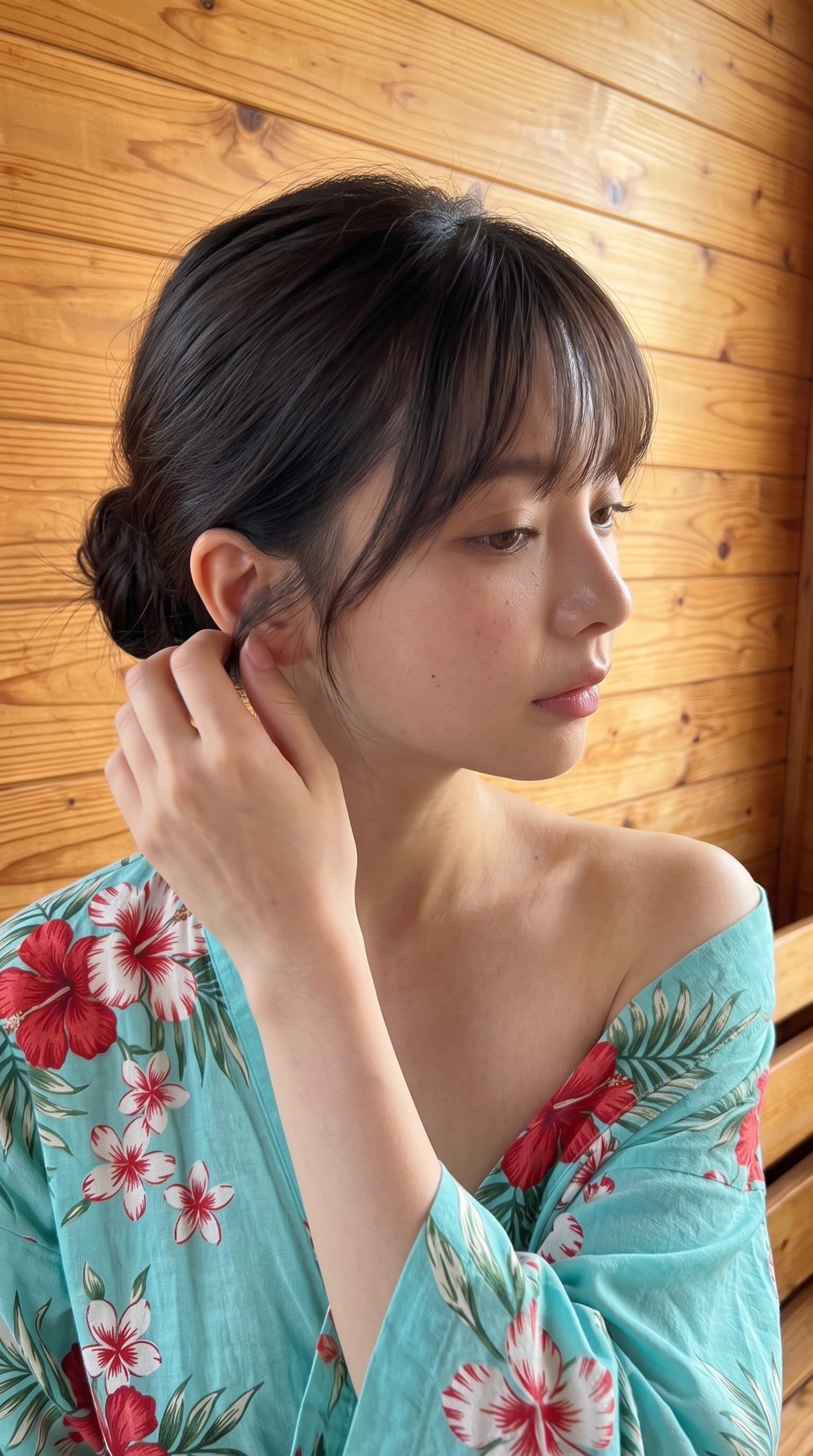 ハイビスカス柄の服を着て、耳元の髪に手を添える黒髪の女性の横顔