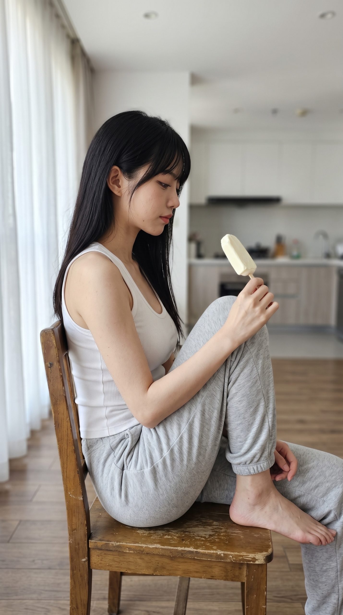 室内で椅子に座り、アイスキャンディーを手にして見つめる黒髪の女性