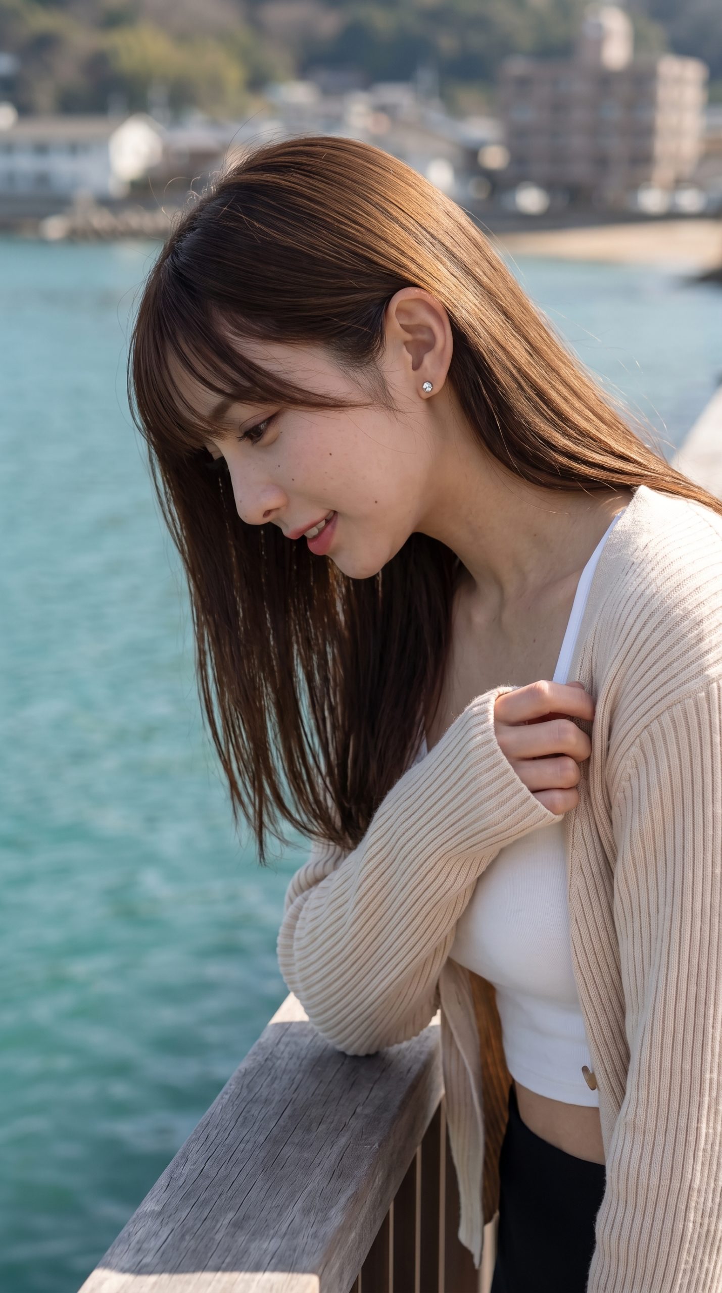 海辺の柵に寄りかかり、穏やかな表情で下を見つめるロングヘアの女性。